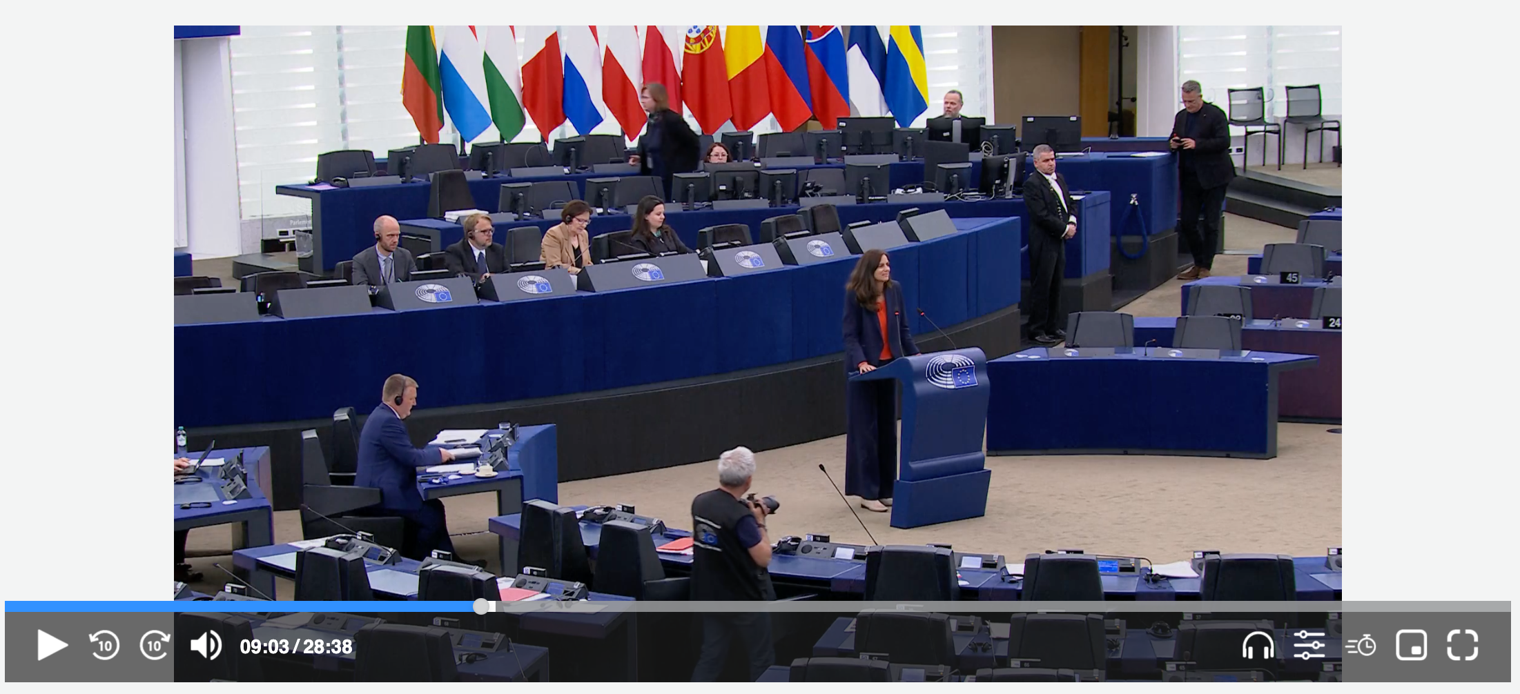 Screenshot of a streaming video player showing a female speaker in the European Parliament